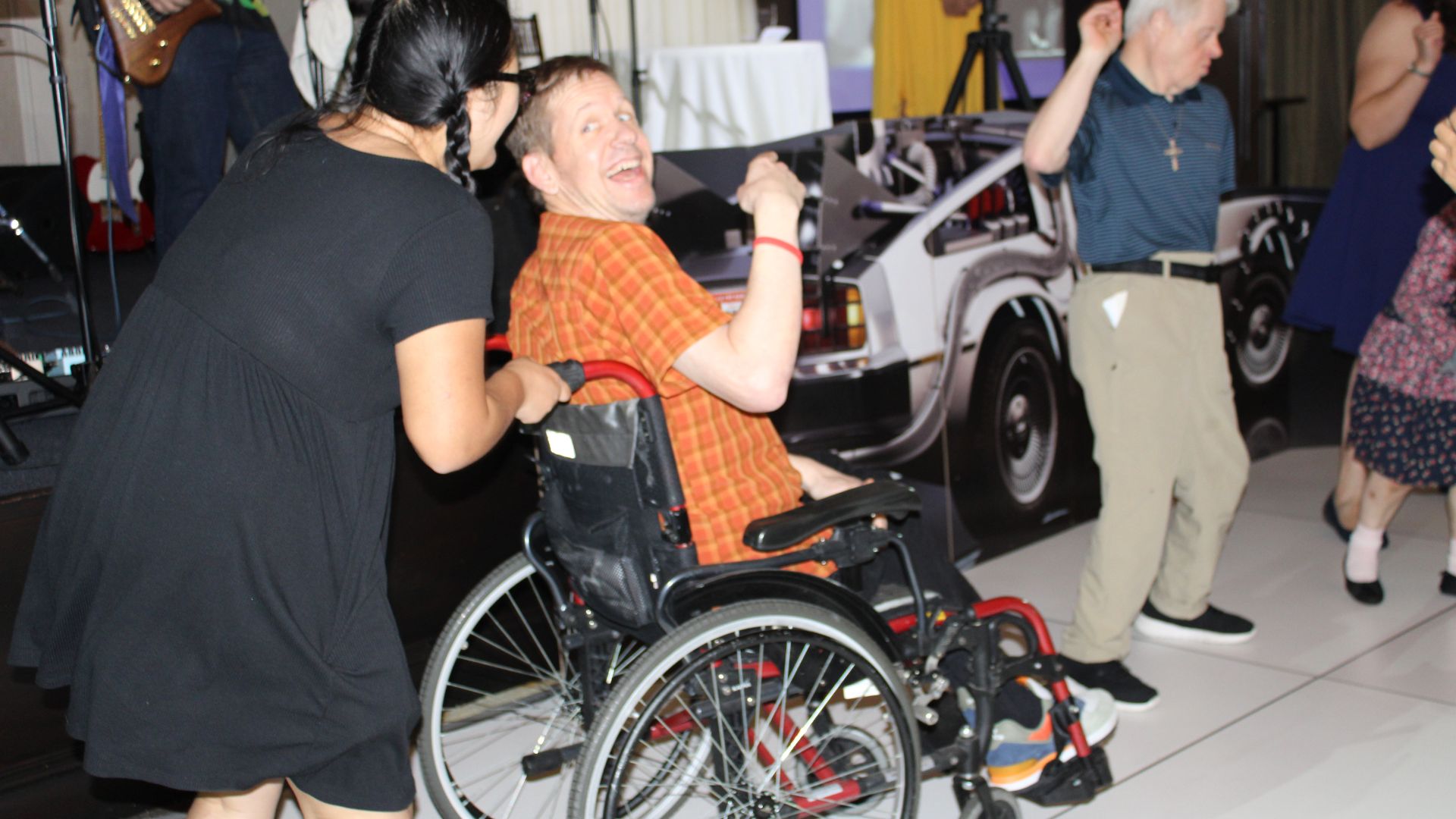 Associates dance in a contest. One in a wheelchair looks over his shoulder smiling at his dance partner.