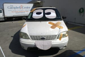 Old white van with googly eye stickers on the windows and bandaids over the hood.
