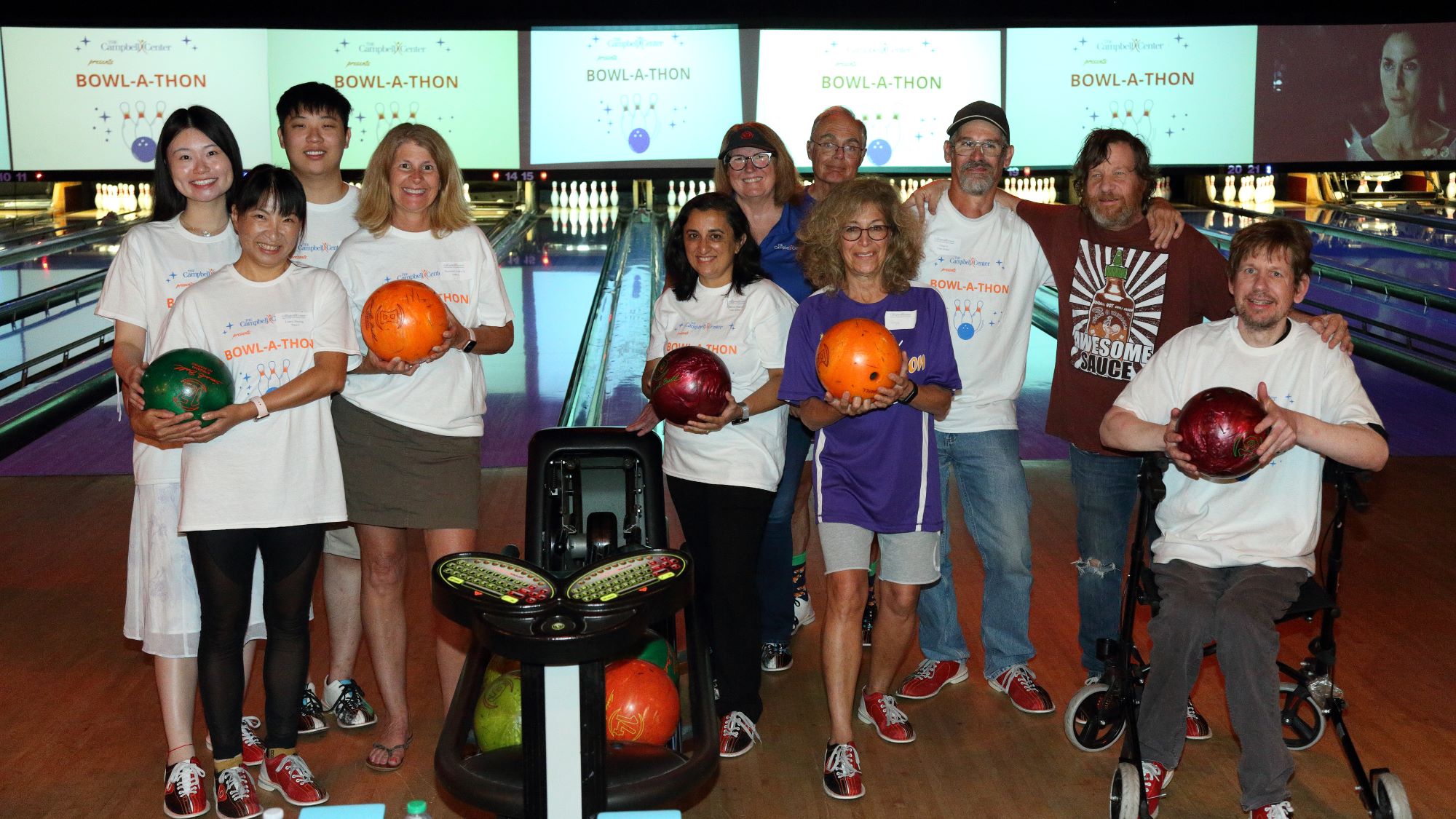 Group photo of bowlers in front of the lanes holding their bowling balls.